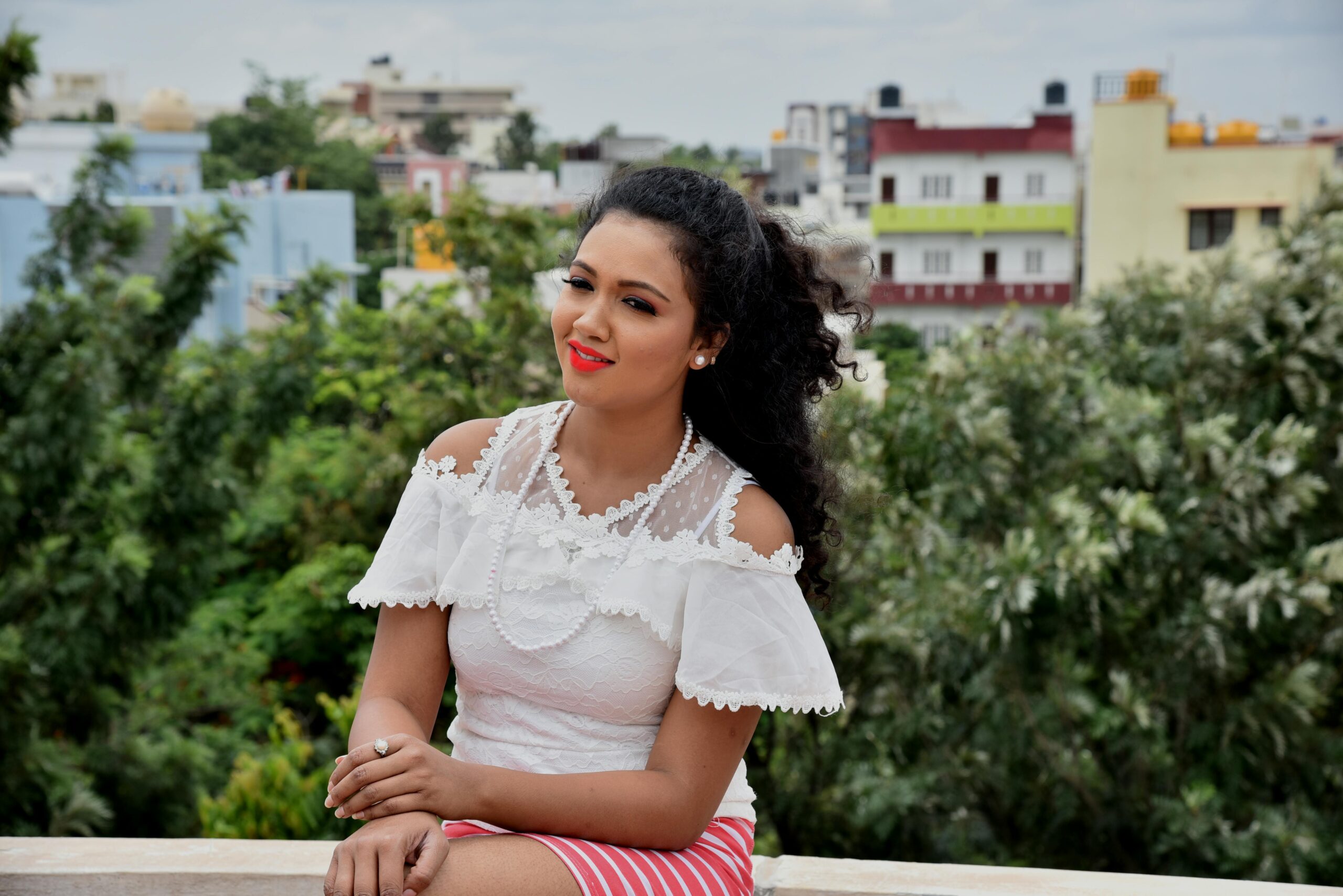 Smiling Woman Sitting on Barrier With Both Hands on Lap